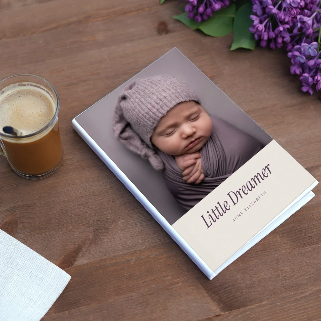 A Little Dreamer book on a wooden table next to coffee and lilacs