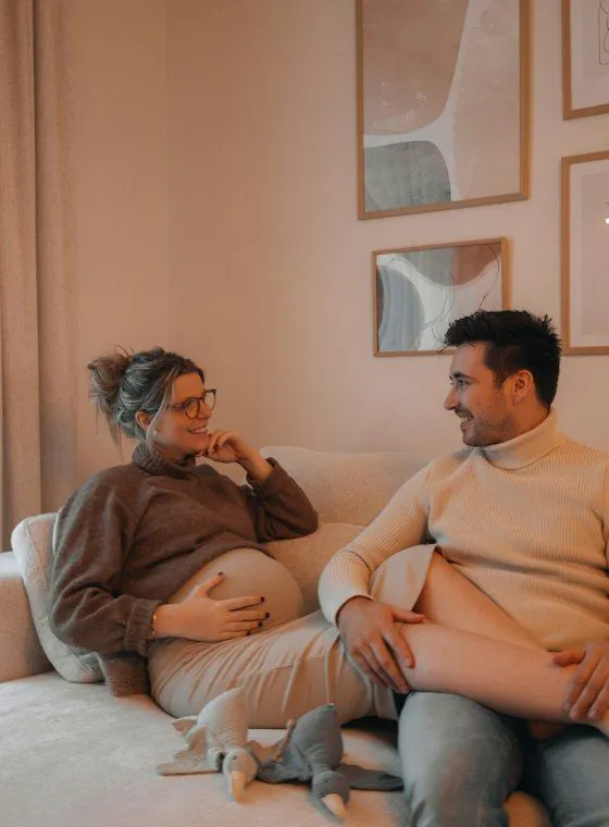 A pregnant woman and her partner laughing on the couch