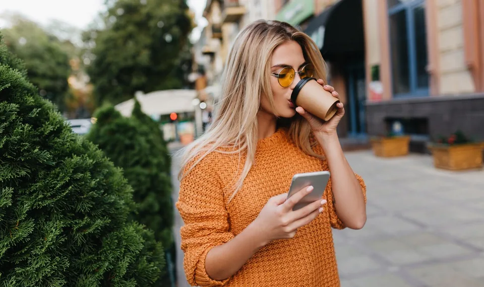 A woman with a coffee checking a new text on her phone