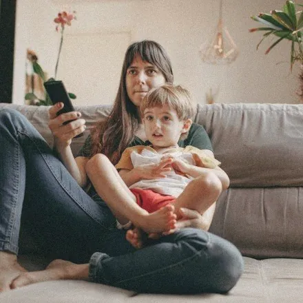 Mom on the sofa with her toddler, reading a text on her phone